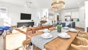 A modern living room with a wooden dining table, leather sofas, and a kitchen area with white cabinets. - Inlet Beach! Sleeps 10, 4 BR/3.5 BA , Pool & just minutes to the beach, Rosemary area and 30Avenue! (Inlet Beach)
