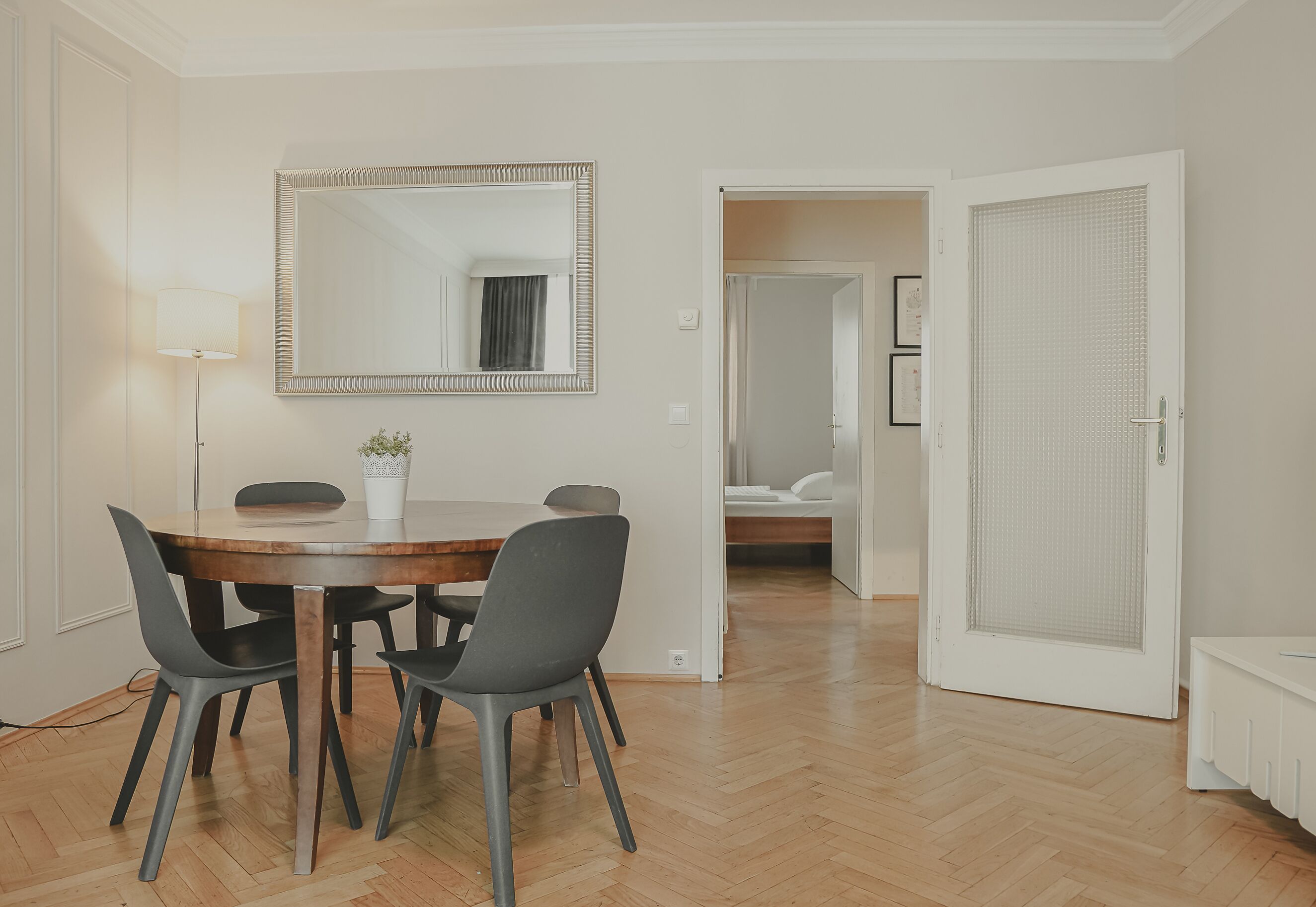 A dining area with a round table, four chairs, a mirror, and a lamp.