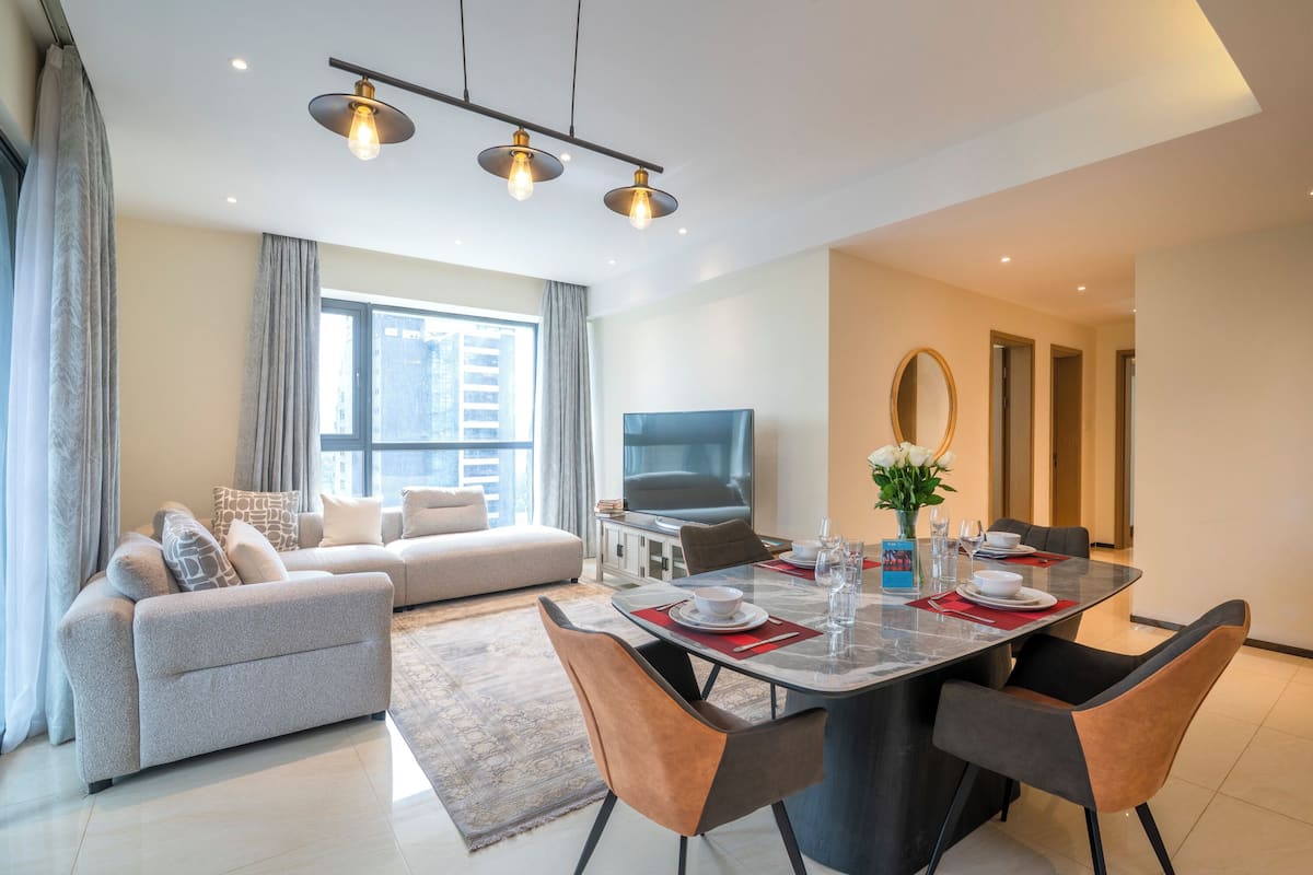 A modern living room with a sofa, dining table, chairs, a TV, and a large window.