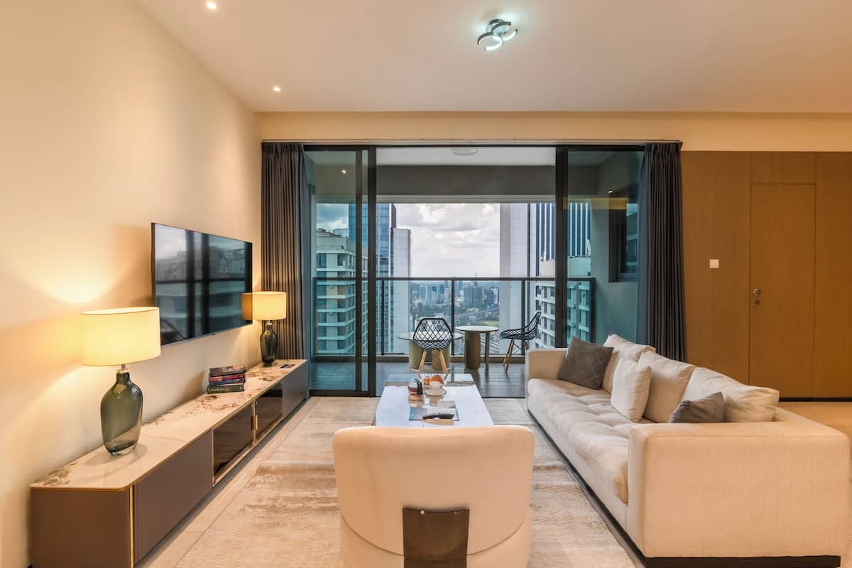 A modern living room with a sofa, coffee table, and TV, a balcony with a city view, and a large window.