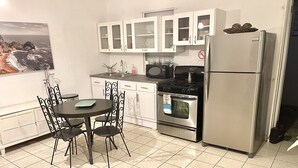 Una cocina con armarios blancos, un refrigerador de acero inoxidable, una estufa y una mesa de comedor con sillas.