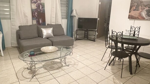 Una sala de estar con sofá, mesa de centro y mesa de comedor con sillas.