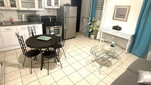 Una cocina compacta con armarios blancos, una mesa de comedor con sillas, un refrigerador y una pequeña planta en maceta.