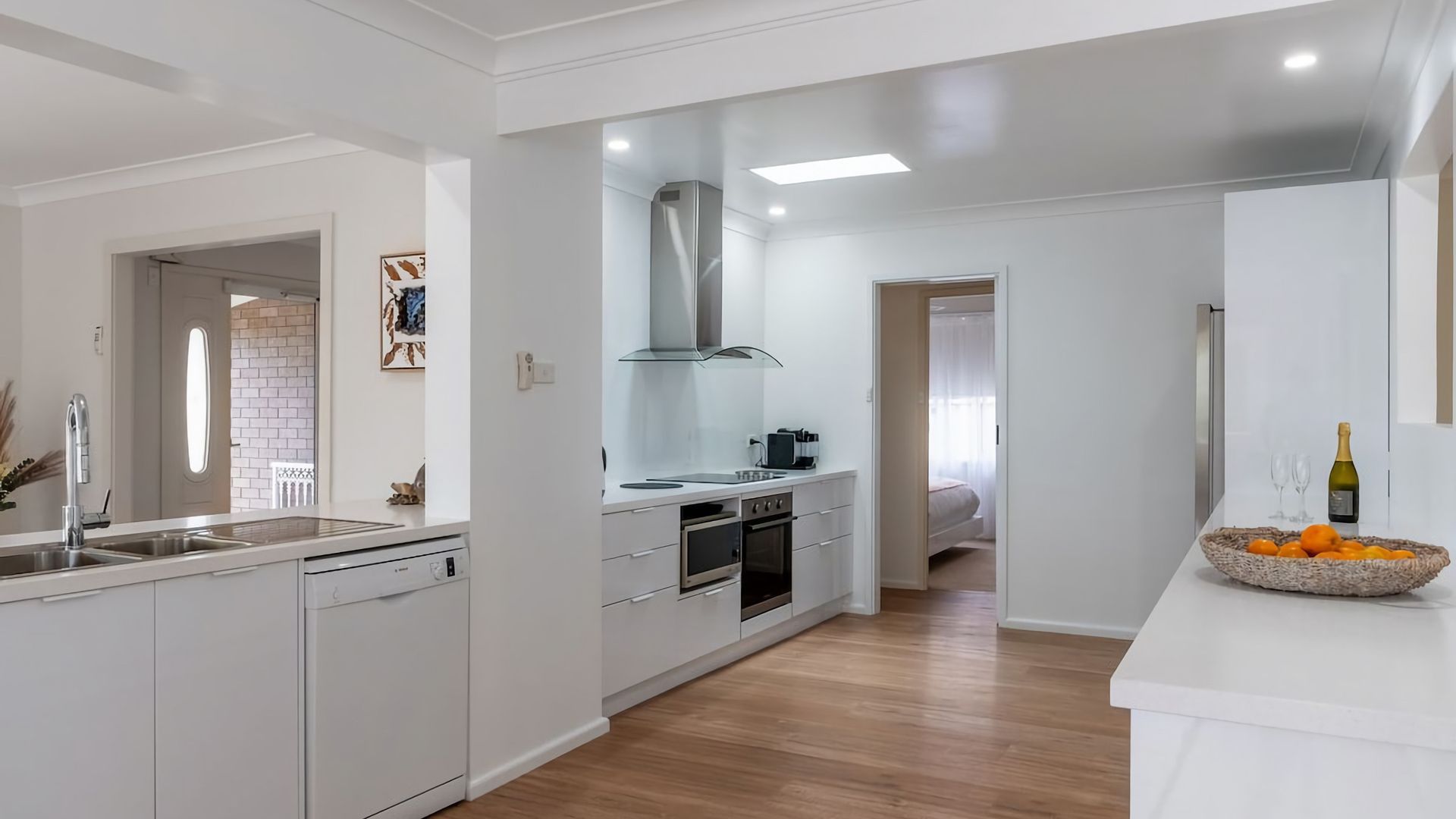 A modern kitchen with white cabinetry, a stainless steel range hood, and a wooden floor.