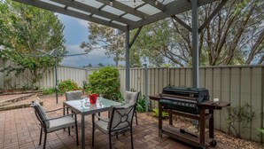 Une terrasse extérieure équipée d’un barbecue, d’une table, de chaises et d’une table dont le plateau est en verre.