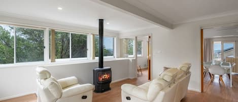 Una sala de estar moderna con chimenea, dos sillones reclinables, un comedor con mesa y sillas, y ventanas amplias con vistas al exterior.