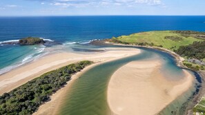 Eine Küstenlandschaft mit Sandstrand, einem grünen Hügel und freiem Blick auf den Ozean.