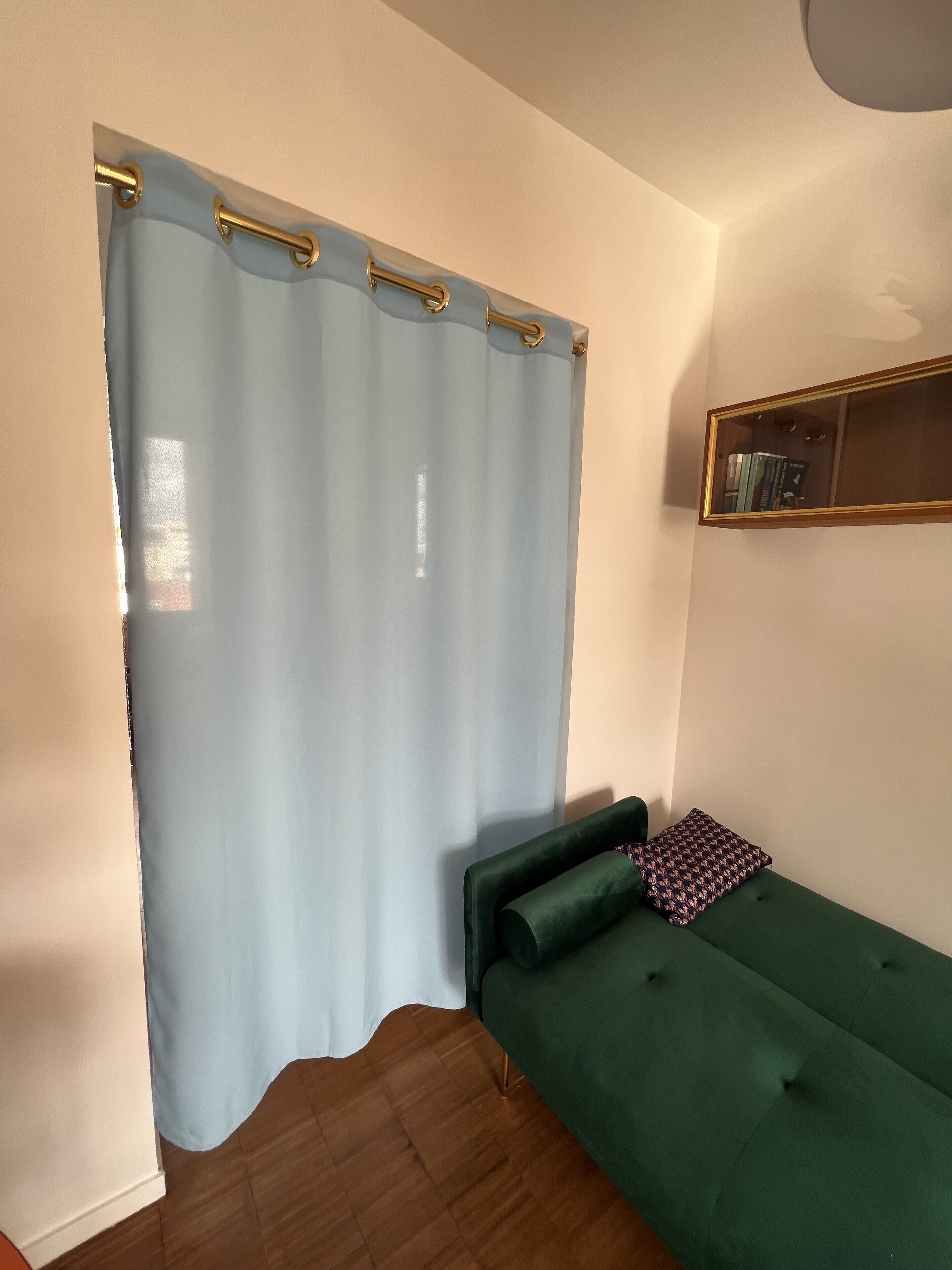 Een kamer met een groene bank, een lichtblauwe gordijn en een houten vloer.