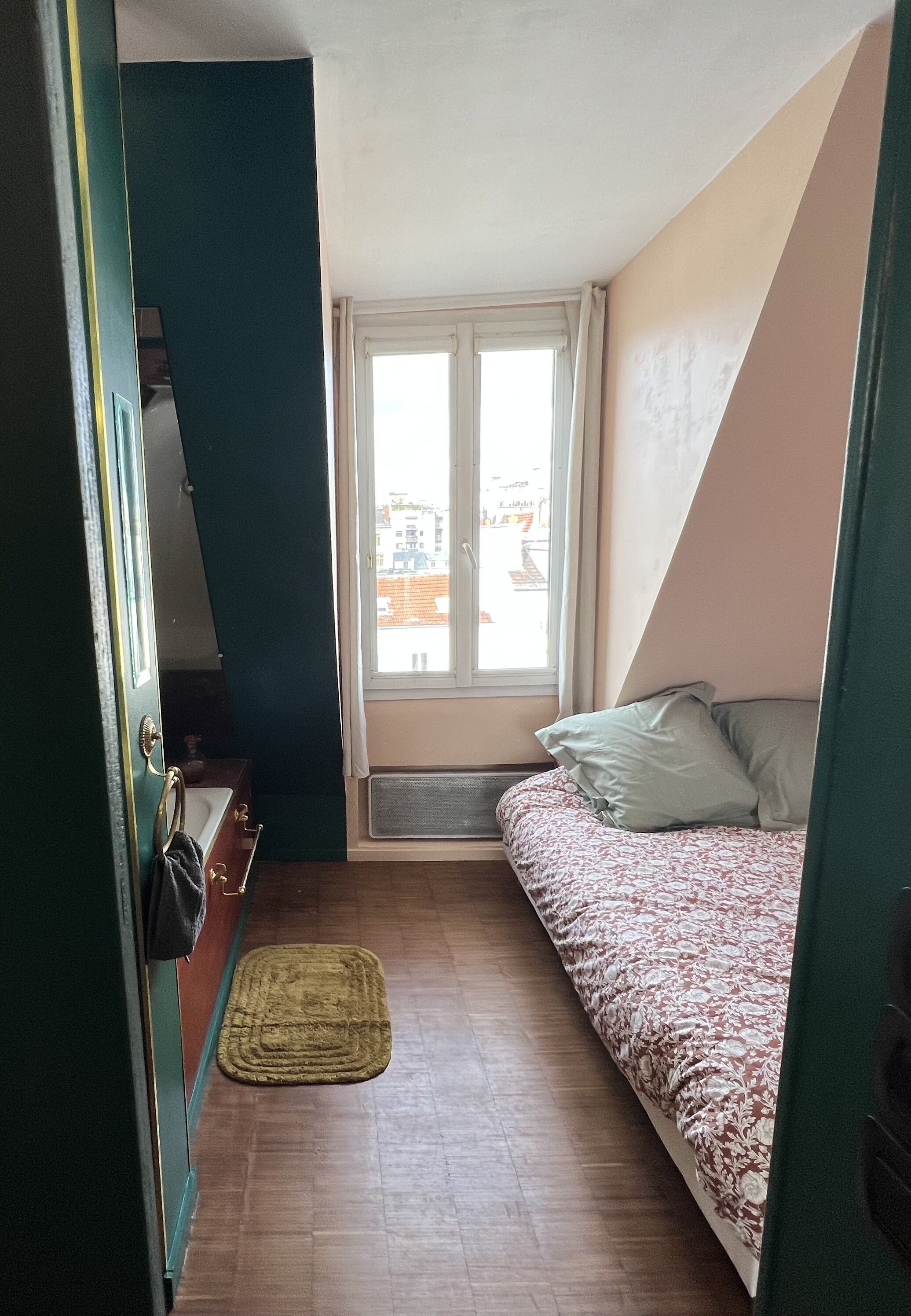 Ein kleiner, schmaler Raum mit einem Bett, einem Fenster und einer Heizung.