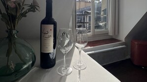 Una botella de vino y dos copas sobre una mesa cerca de una ventana con vistas a edificios.