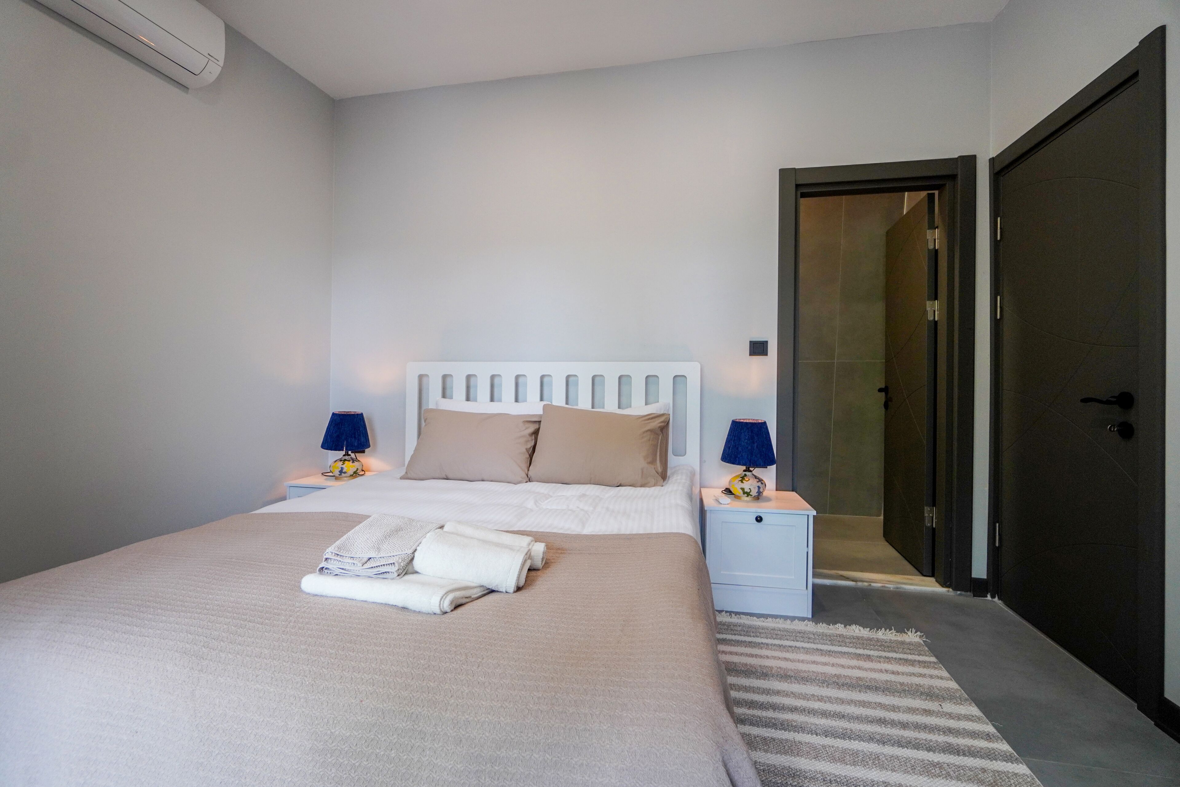 Een netjes opgemaakt bed met een wit hoofdeinde, twee bedlampen en een opgevouwen handdoek op het bed.