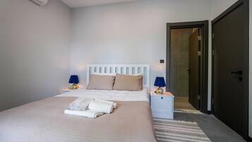 Een netjes opgemaakt bed met een wit hoofdeinde, twee bedlampen en een opgevouwen handdoek op het bed.