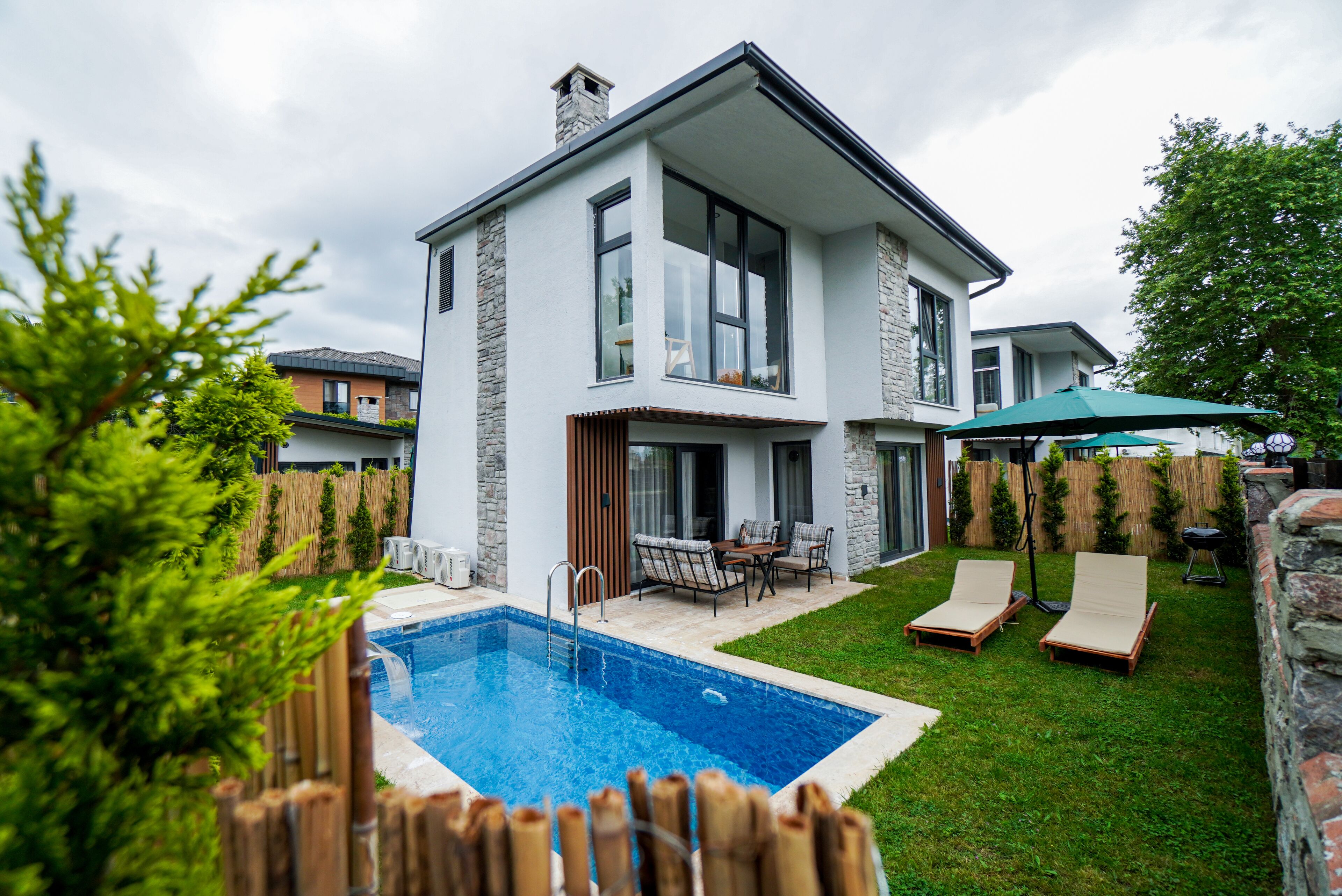 A modern two-story house with a swimming pool, outdoor furniture, and a wooden fence.