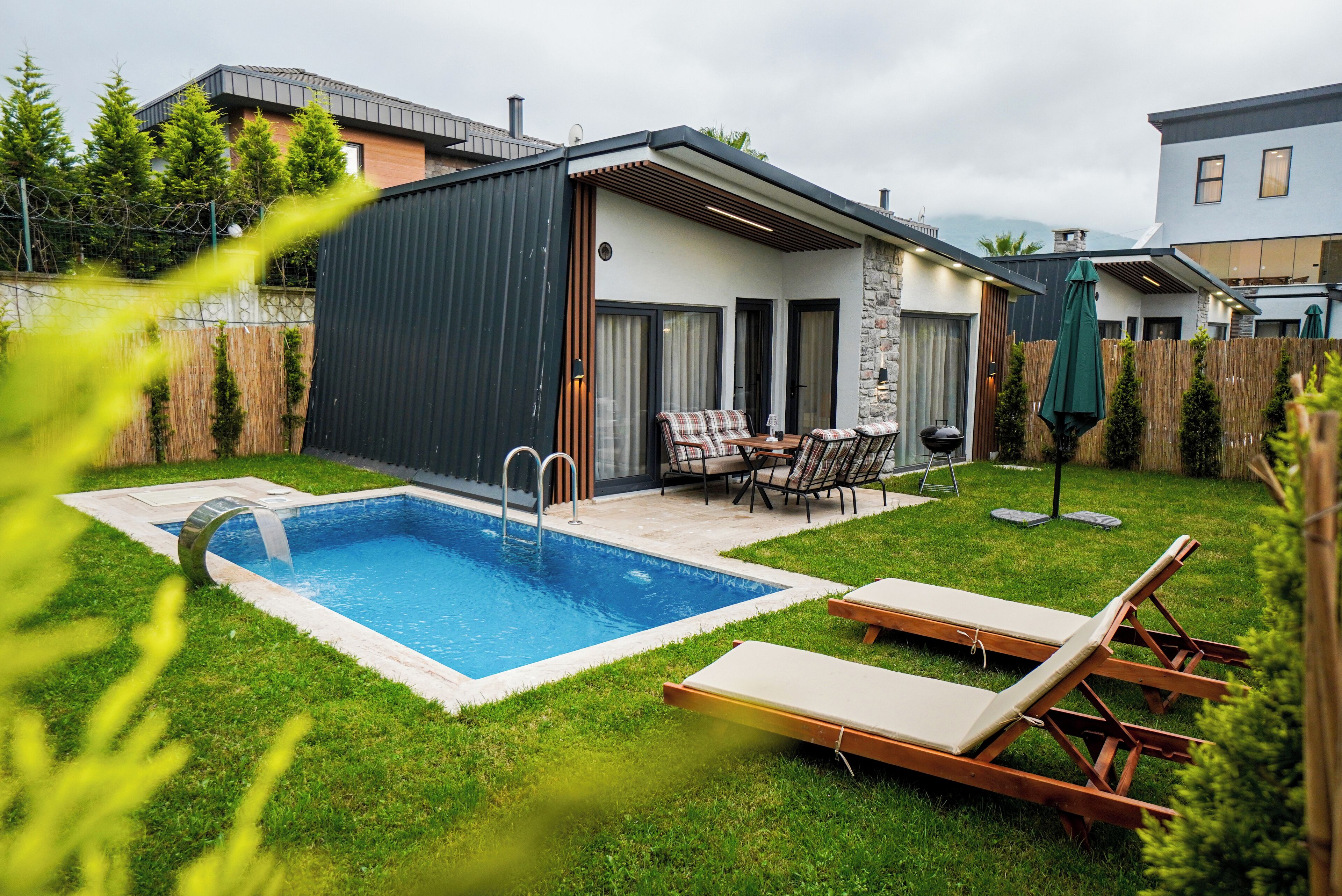 A modern house with a swimming pool, outdoor seating, and a well-maintained lawn.