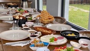 A dining table set for a meal with various dishes, including bread, salad, and meats, in a room with a large window and a view of the outdoors. - Vital Home (Sapanca)