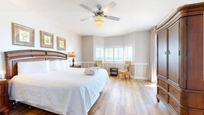 Un dormitorio amplio con una cama grande, un ventilador de techo y vistas al mar a través de las ventanas.