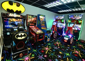 Une salle avec des jeux d’arcade, notamment des jeux Batman et des jeux de course, et un sol orné de motifs en forme d’étoiles.