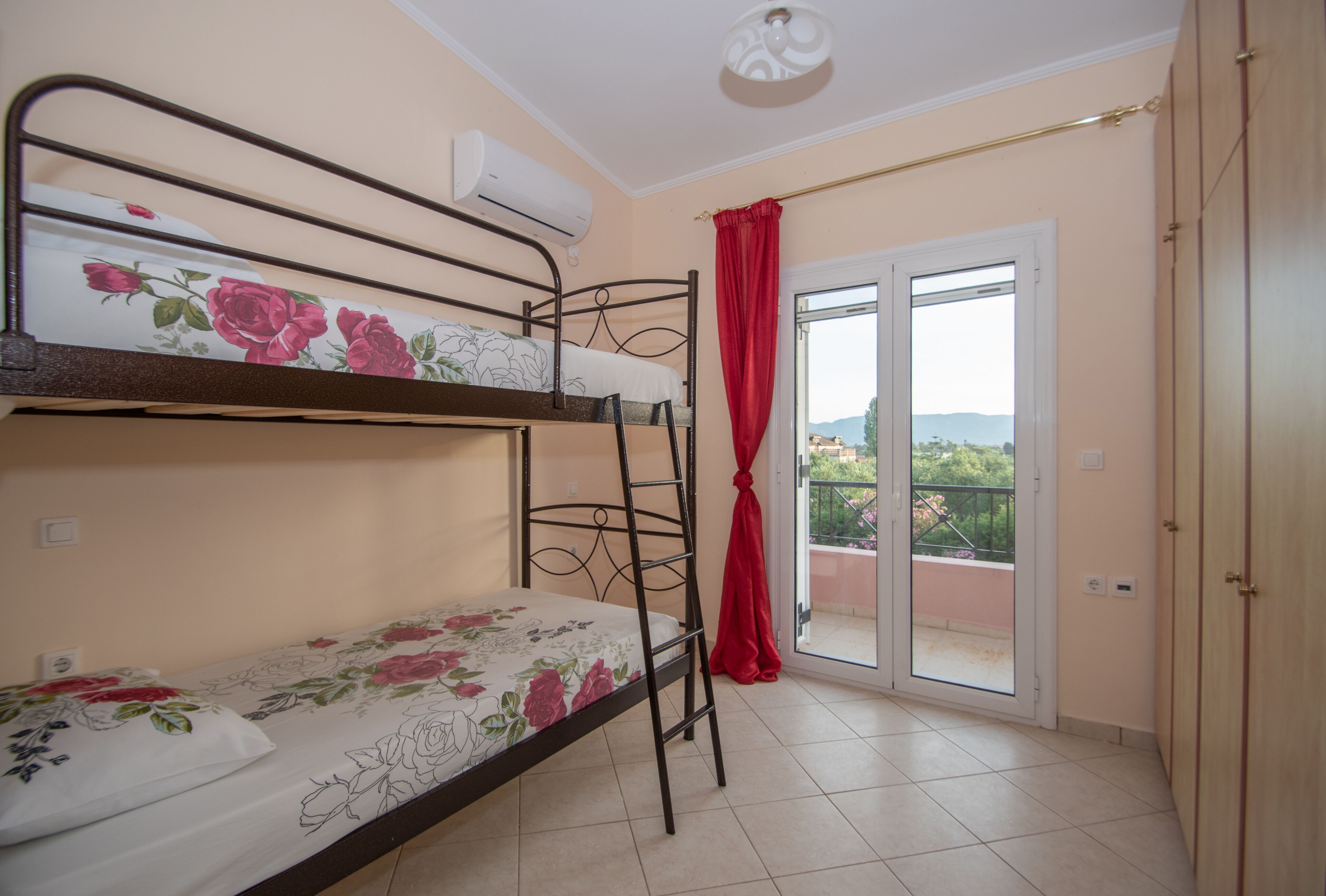 A dormitory room with bunk beds, a sliding glass door to a balcony, and a ceiling fan.