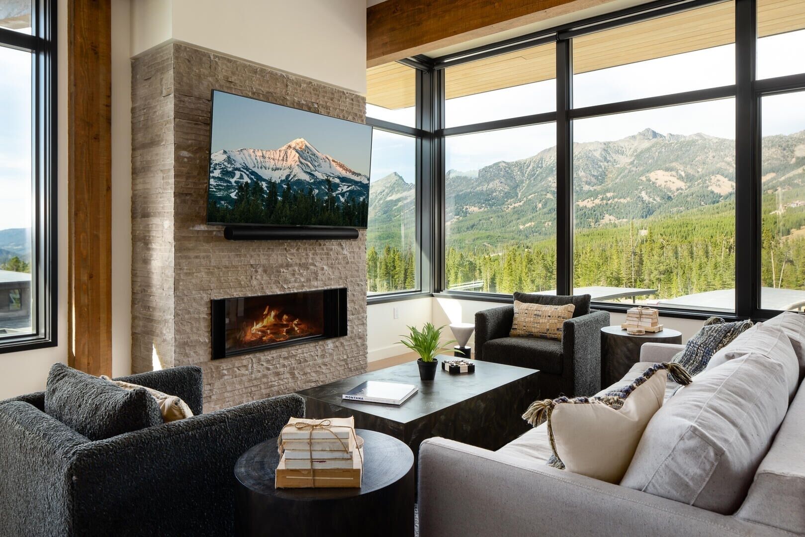 A modern living room with a stone fireplace, comfortable seating, and a large window offering a mountain view.