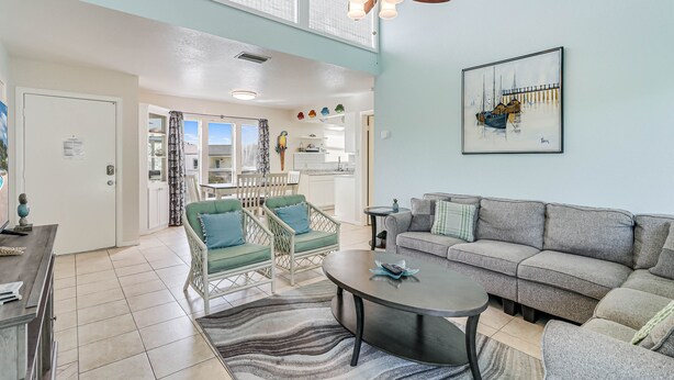 A spacious living area with a large gray sofa, a round coffee table, and a dining area with a white table and chairs.