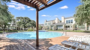 A wooden deck with a swimming pool, lounge chairs, and a pergola.