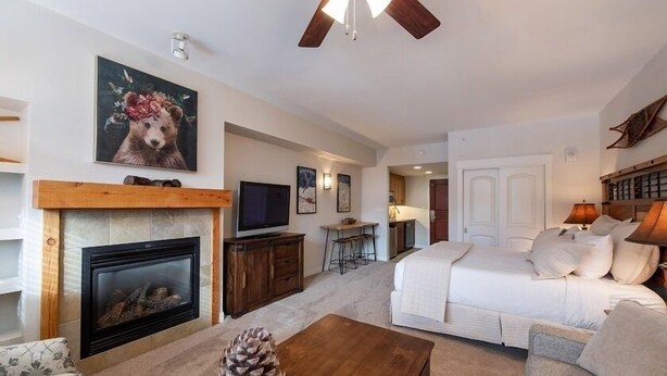 A spacious living room with a fireplace, a television, and a bed with a large window. - Premium Unit 4643- Fraser Crossing/founders Pointe Condo (Winter Park)