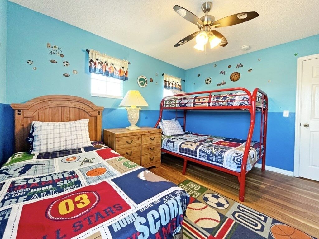 A bedroom with a bunk bed, a wooden nightstand, a lamp, and sports-themed decorations.