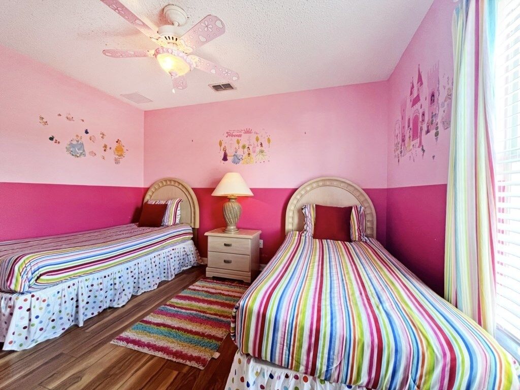 A bedroom with two beds, a ceiling fan, a nightstand, and a window with curtains.