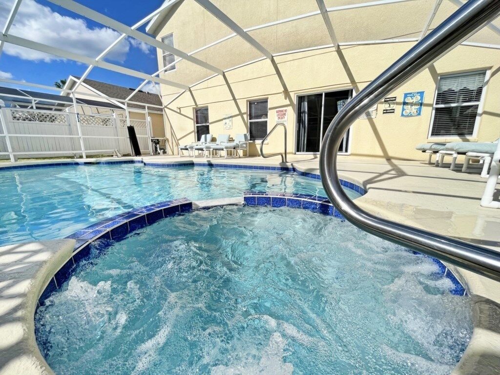 A pool area with a hot tub, lounge chairs, and a covered patio.