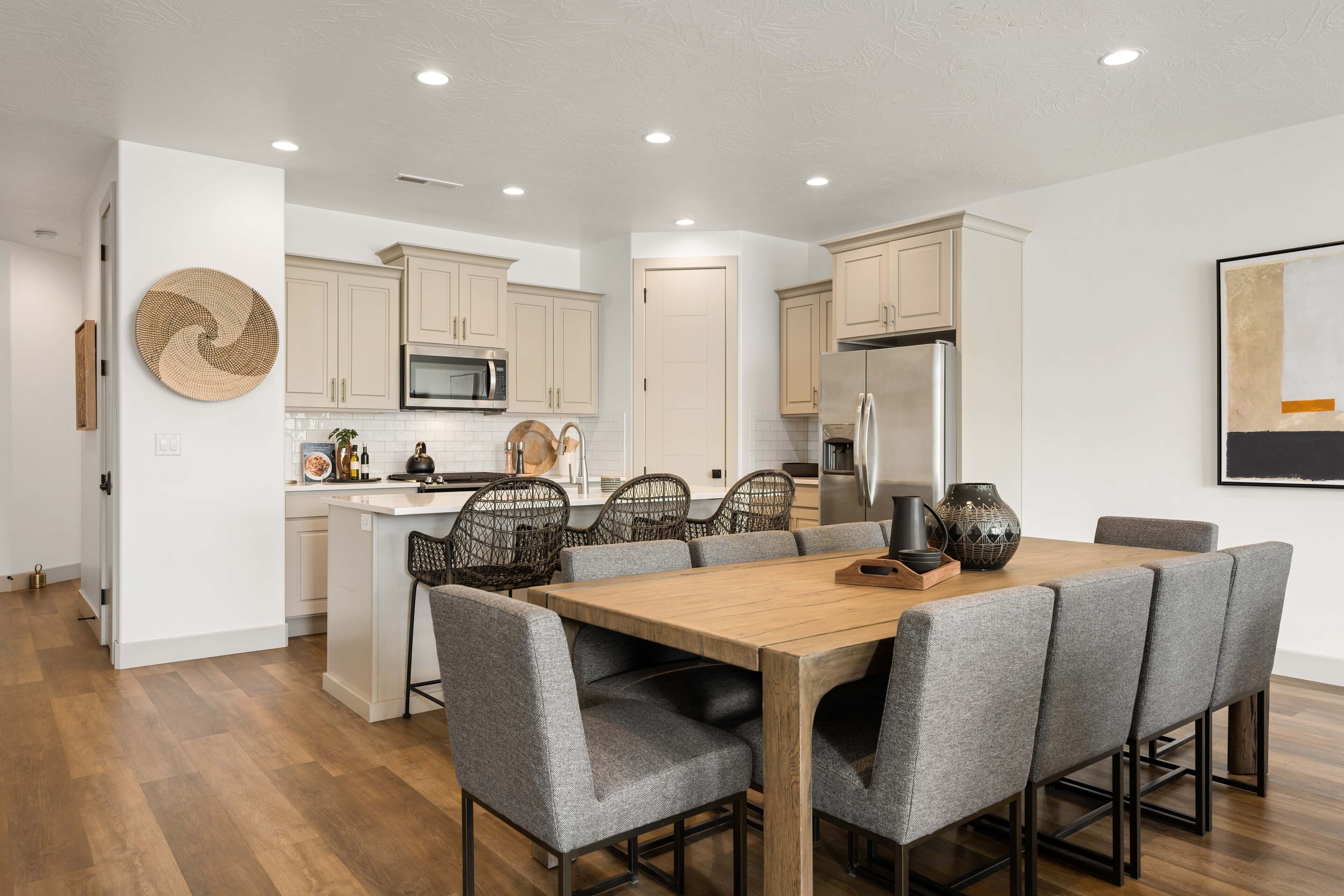 A modern kitchen with wooden cabinets, a central island, and a dining area with grey upholstered chairs.