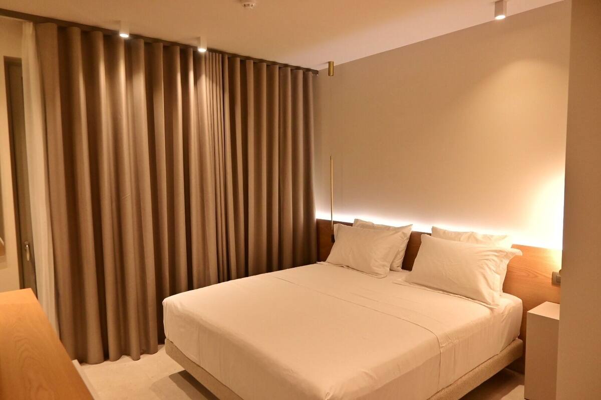 A hotel room with a large bed, a nightstand, and a curtain-covered window.