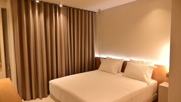 Una habitación de hotel con una cama grande, una mesita de noche y una ventana cubierta por cortinas.