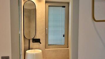 Un baño moderno con puerta de cristal, espejo redondo, lavabo e inodoro.