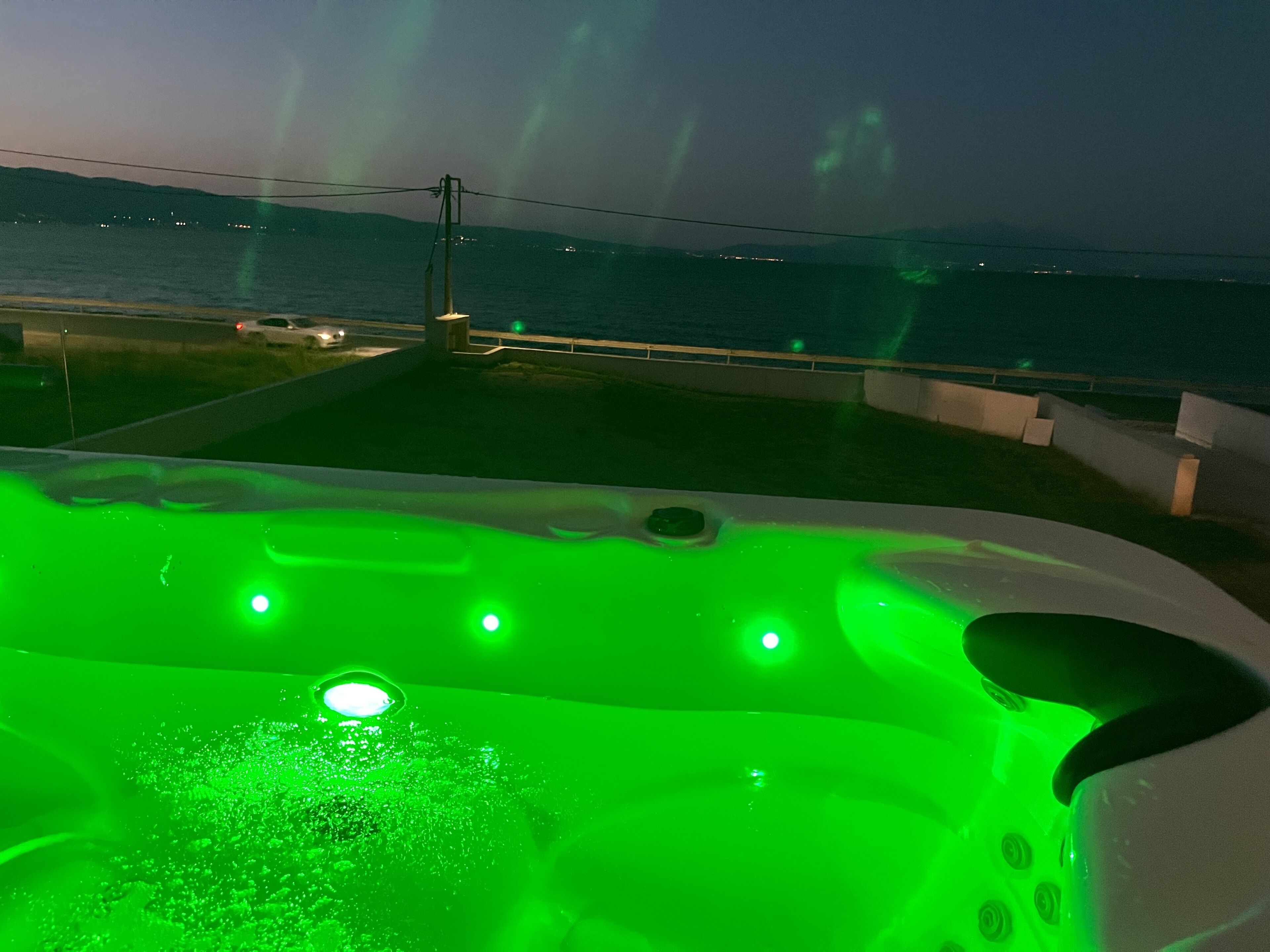 Un jacuzzi con iluminación verde, vista al mar y una cadena montañosa distante.