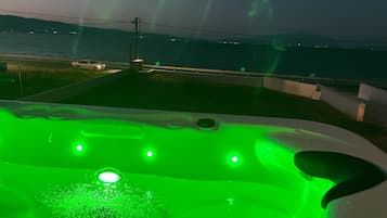 Un jacuzzi con iluminación verde, vista al mar y una cadena montañosa distante.