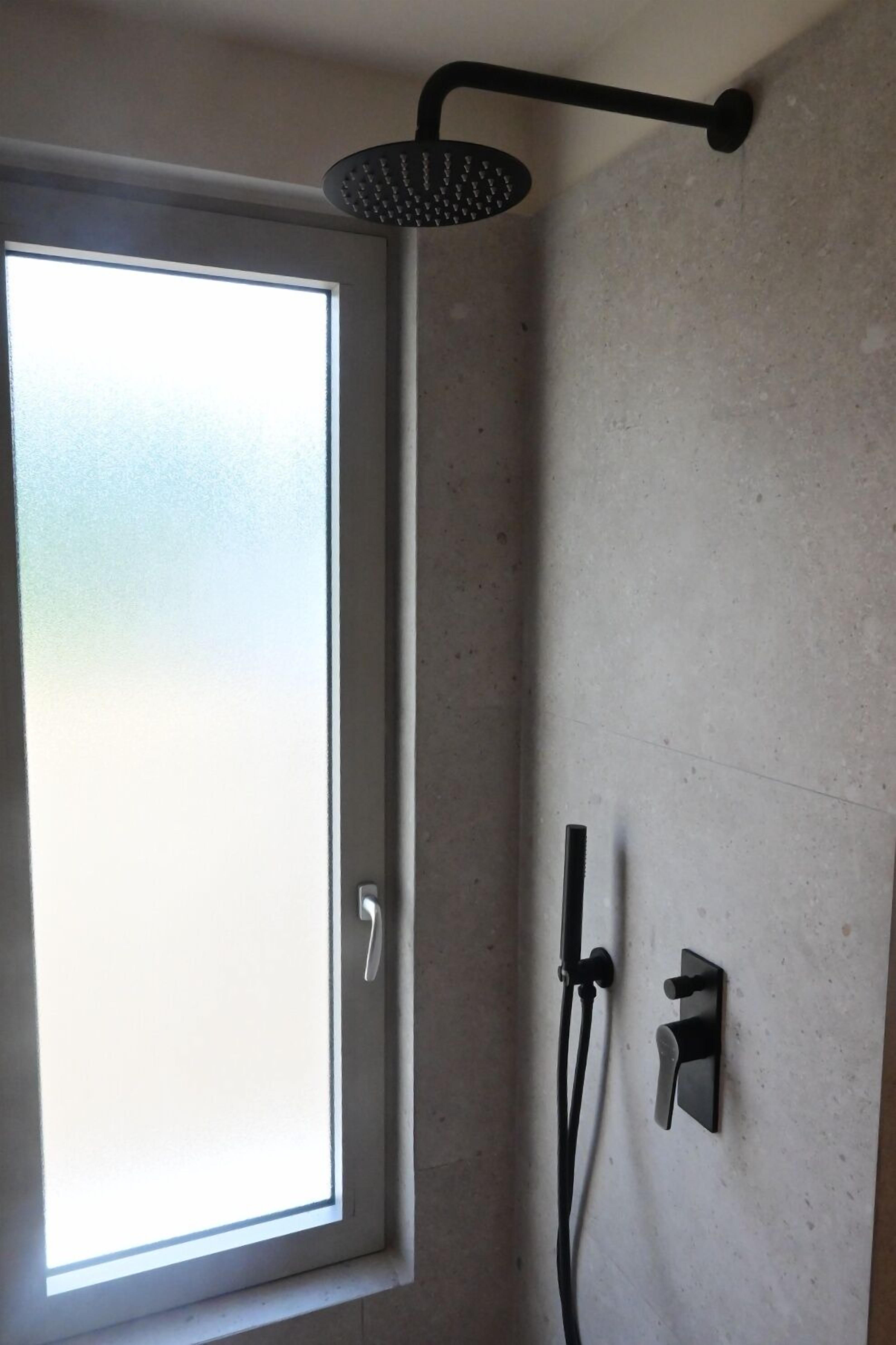 Eine Dusche mit einer Handbrause, die an der Wand befestigt ist, ein Fenster mit Milchglas und eine Tür mit Griff.