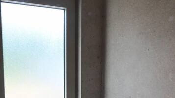 Eine Dusche mit einer Handbrause, die an der Wand befestigt ist, ein Fenster mit Milchglas und eine Tür mit Griff.