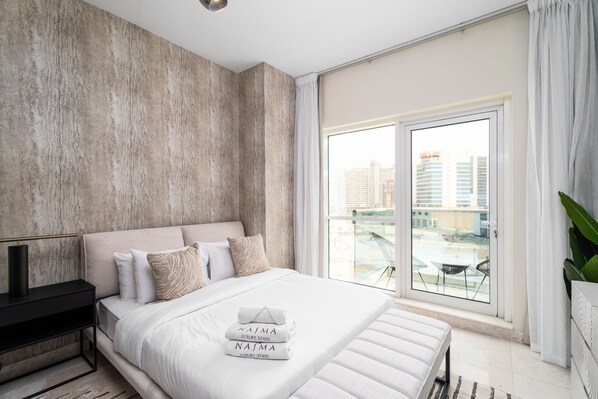 A modern bedroom with a large bed, a view of the city through a floor-to-ceiling window, and a balcony with a view. - Nasma Holiday Homes - Safeer Tower 1 (Dubai)