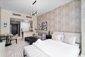 Quarto de hotel moderno com uma cama grande, um sofá, uma mesa de centro e uma área de refeições com cadeiras.
