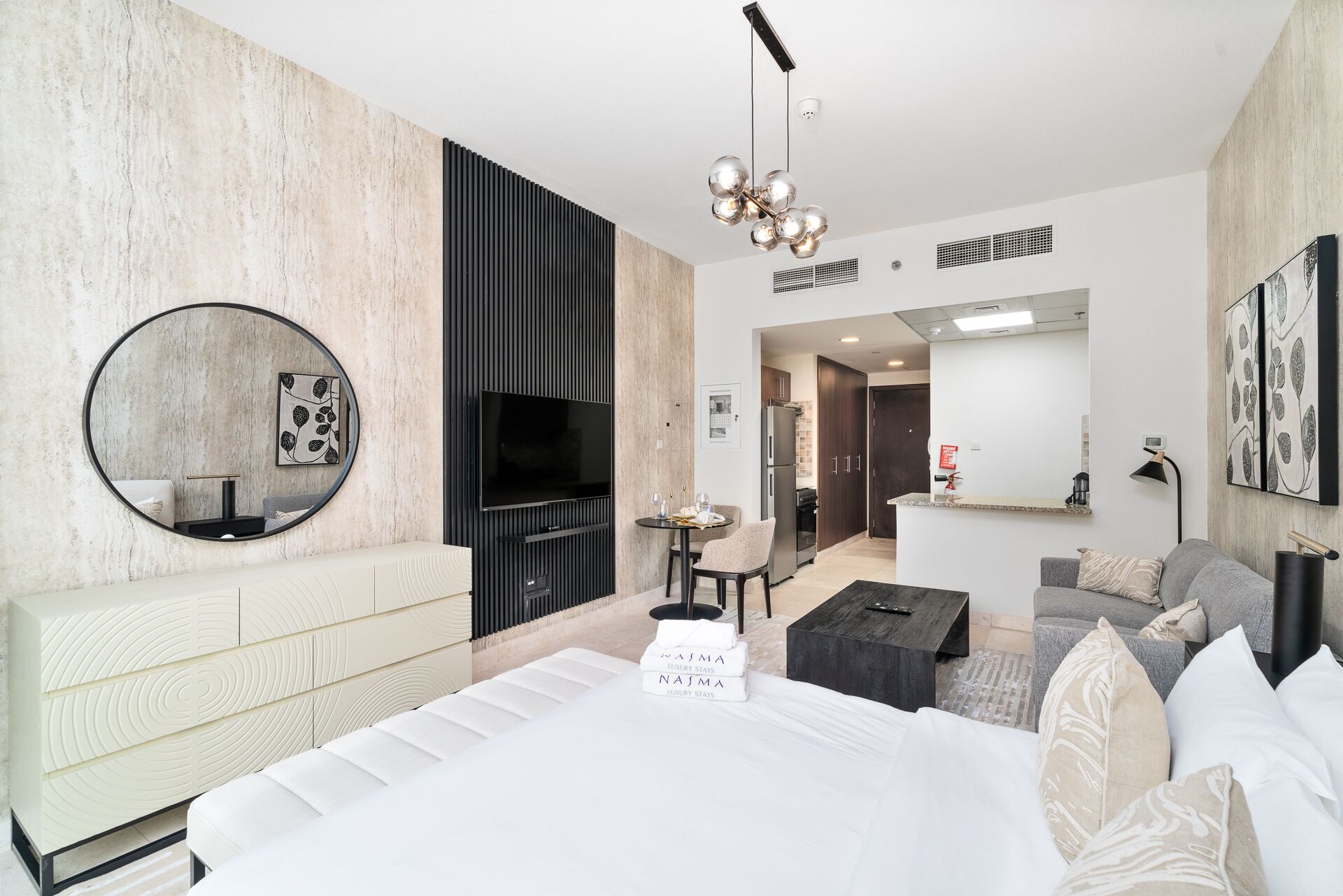 Een moderne hotelkamer met een groot bed, een televisie, een ronde spiegel en een zithoek met een tafel en stoelen.