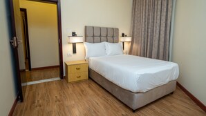 Een hotelkamer met een bed, nachtkastjes en een deur naar een andere kamer.