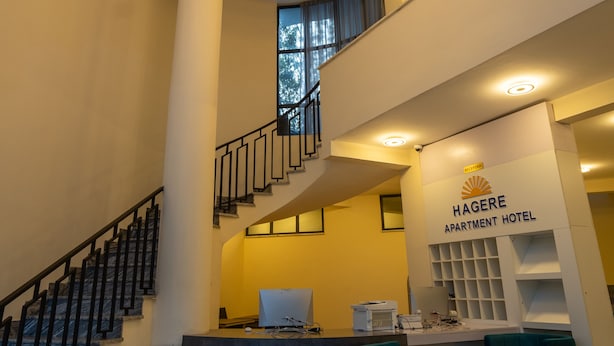 Een modern interieur van Hagere Apartment Hotel, met een receptiebalie, zithoek en een trap.