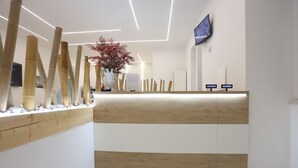 A reception desk with a wooden finish, a vase with red flowers, and a flat-screen TV mounted on the wall. - PALAZZO SANT'ARCANGELO (Naples)