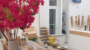 A buffet setup with various food items, a vase of pink flowers, and a television mounted on the wall. - PALAZZO SANT'ARCANGELO (Naples)
