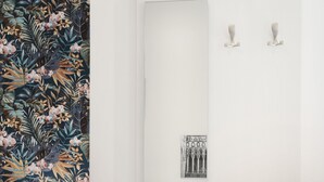 A modern hotel room with a floral wallpaper, a wooden side table, a white desk, a green pillow, and a vase with flowers. - PALAZZO SANT'ARCANGELO (Naples)