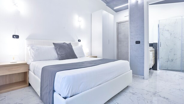 A modern bedroom with a bed, bedside tables, and a walk-in closet. - PALAZZO SANT'ARCANGELO (Naples)