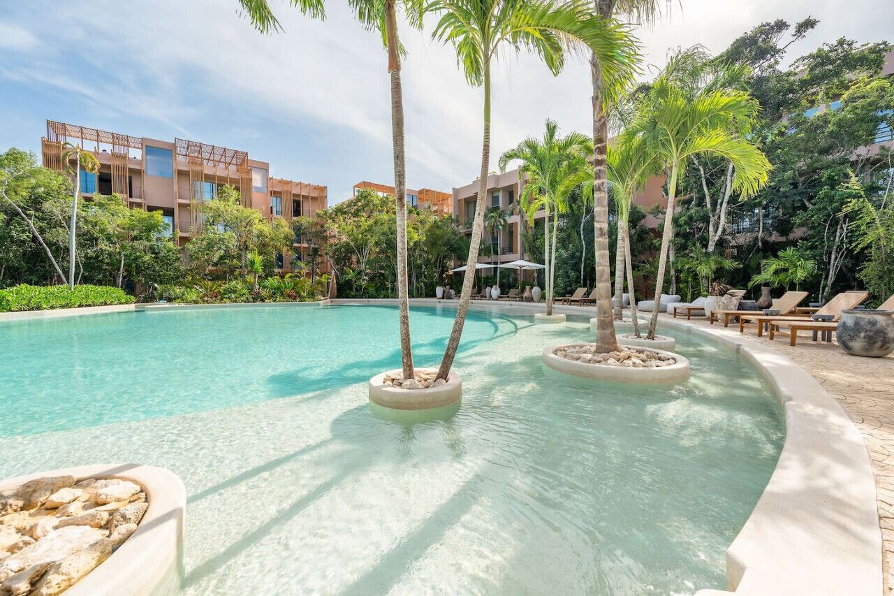 A swimming pool with lounge chairs, palm trees, and a building in the background.