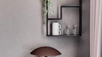 Una habitación moderna con un escritorio de madera, una lámpara marrón, una estantería negra con una planta, una taza blanca y una cafetera.