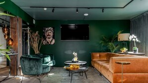 A modern living room with a green accent wall, a large flat-screen TV, a green velvet sofa, a round coffee table, and a tall floor lamp.