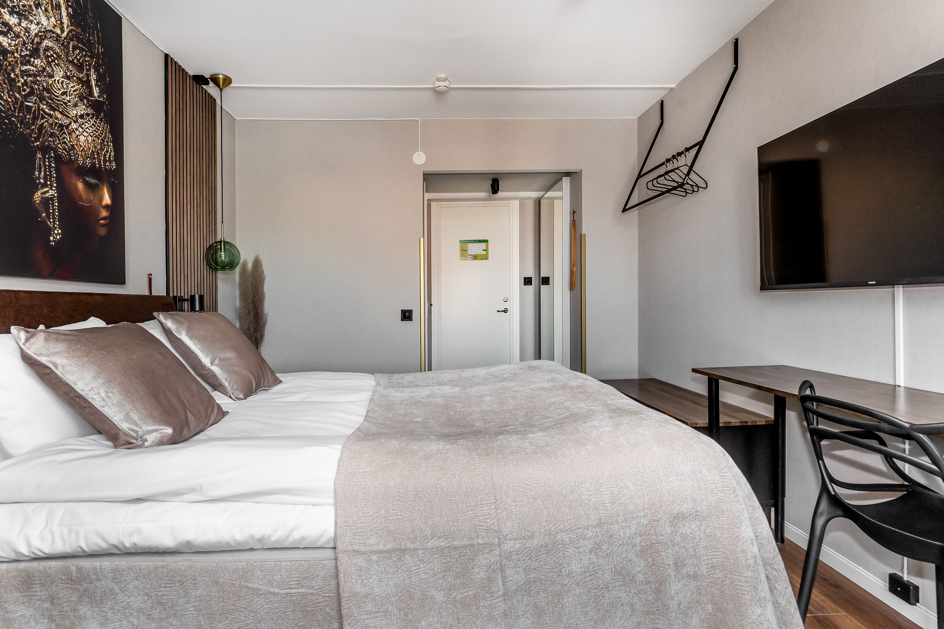 A modern hotel room with a large bed, a desk, and a flat-screen TV on the wall.